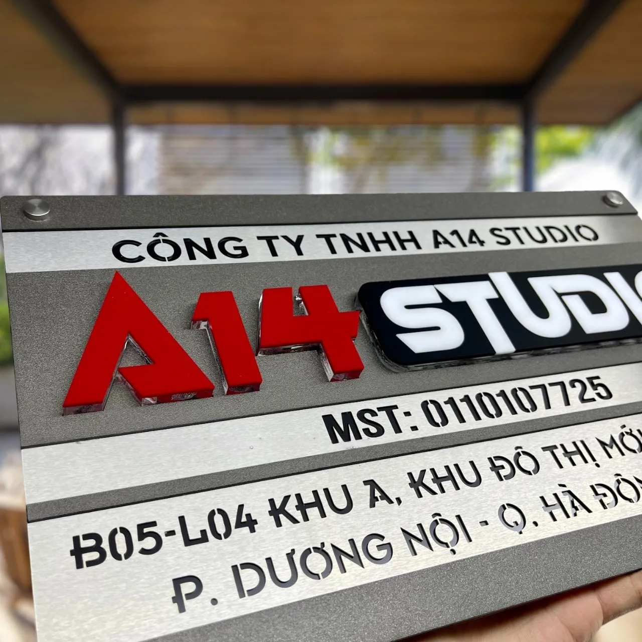 Bảng hiệu công ty inox xám khói chữ nổi 3D đa màu phối cảnh toàn cảnh ngoài trời Toàn cảnh bảng hiệu công ty inox 2 lớp xám khói xước bạc chữ nổi 3D đa màu cầm tay phối cảnh không gian mở ngoài trời