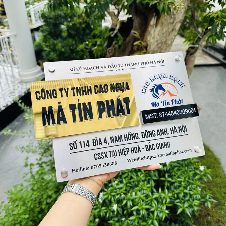 Bảng hiệu công ty inox 304 xước bạc khối tên thương hiệu vàng gương chữ nổi 3D đặt phẳng trên nền gỗ tối