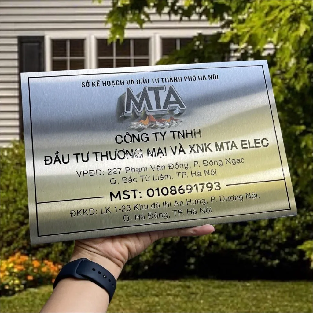 Toàn cảnh bảng hiệu công ty inox trắng xước in UV màu sắc tùy chỉnh, logo MTA chrome, chữ đen sắc nét, khung viền chìm, nền dày 15mm