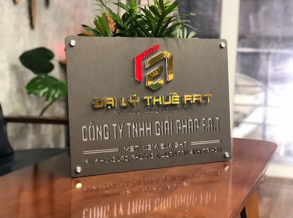 Bảng hiệu công ty inox xám khói logo 3D góc nghiêng 45 độ trên bàn văn phòng Bảng hiệu công ty inox xám khói logo nổi 3D vàng đỏ bạc nhìn góc nghiêng 45 độ trên mặt bàn gỗ