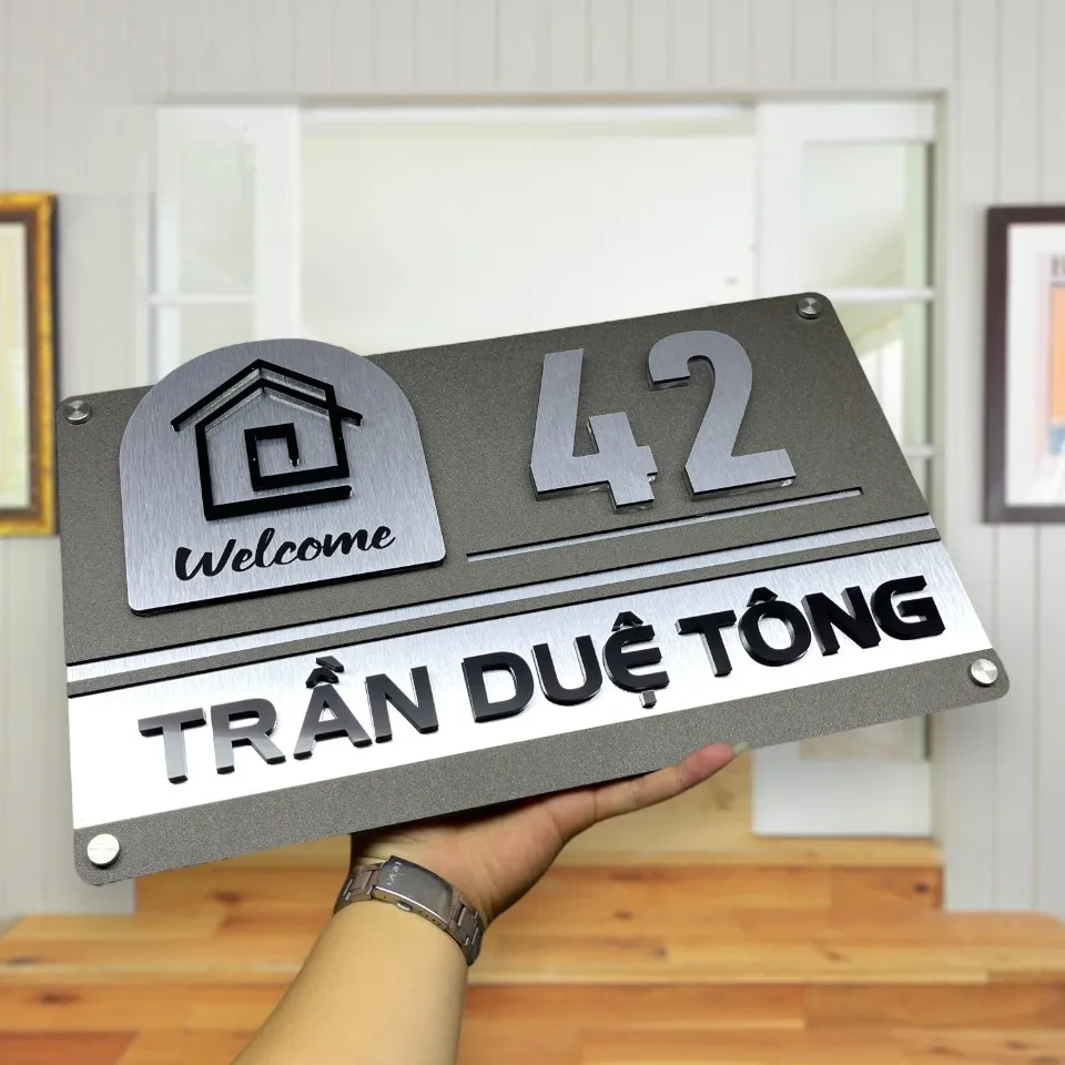 Chi tiết họa tiết ngôi nhà và chữ Welcome trên bảng số nhà inox 304 Close-up biểu tượng ngôi nhà inox đen cách điệu và chữ Welcome thủ bút trên bảng số nhà