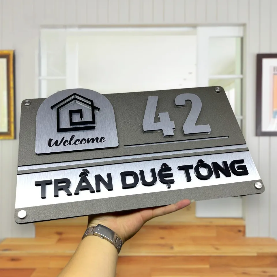 Bảng số nhà inox 304 xước bạc trên nền gỗ – hình ảnh toàn cảnh sản phẩm Toàn cảnh bảng số nhà inox 304 xước bạc chữ nổi 3D mẫu Welcome đặt trên nền gỗ sáng
