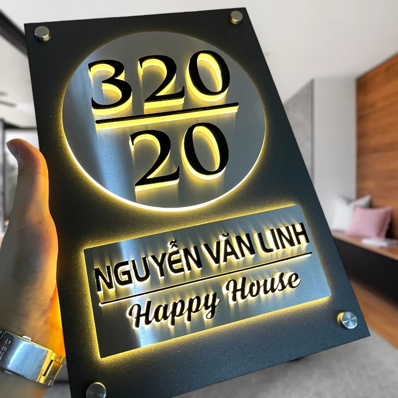 Bảng số nhà inox sơn tĩnh điện họa tiết tròn chữ nổi LED halo vàng ấm — cầm tay góc nghiêng Bảng số nhà inox sơn tĩnh điện tấm tròn chữ nổi inox trên mica LED halo vàng ấm cầm tay