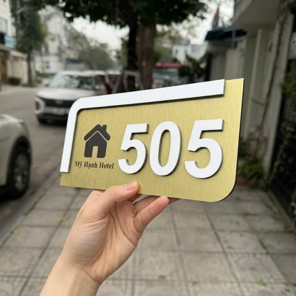 Cận cảnh logo in UV trên bảng số phòng inox Chi tiết logo in UV màu xám đen trên nền inox vàng đồng