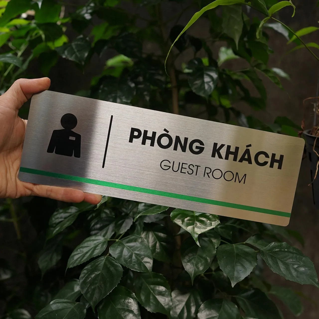 Bảng tên phòng khách inox 304 phay xước cầm tay mặt trước nền cây xanh đậm