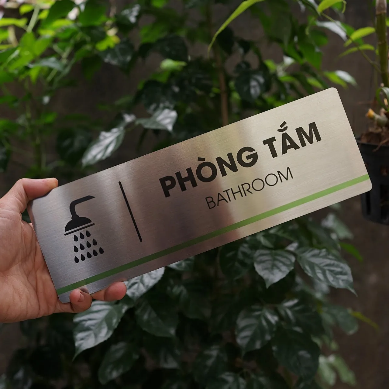 Bảng tên phòng tắm inox 304 cầm tay góc nghiêng – thấy rõ hiệu ứng phay xước và sọc màu Bảng tên phòng tắm inox 304 cầm tay góc nghiêng nhẹ thấy rõ bề mặt phay xước và sọc xanh lá