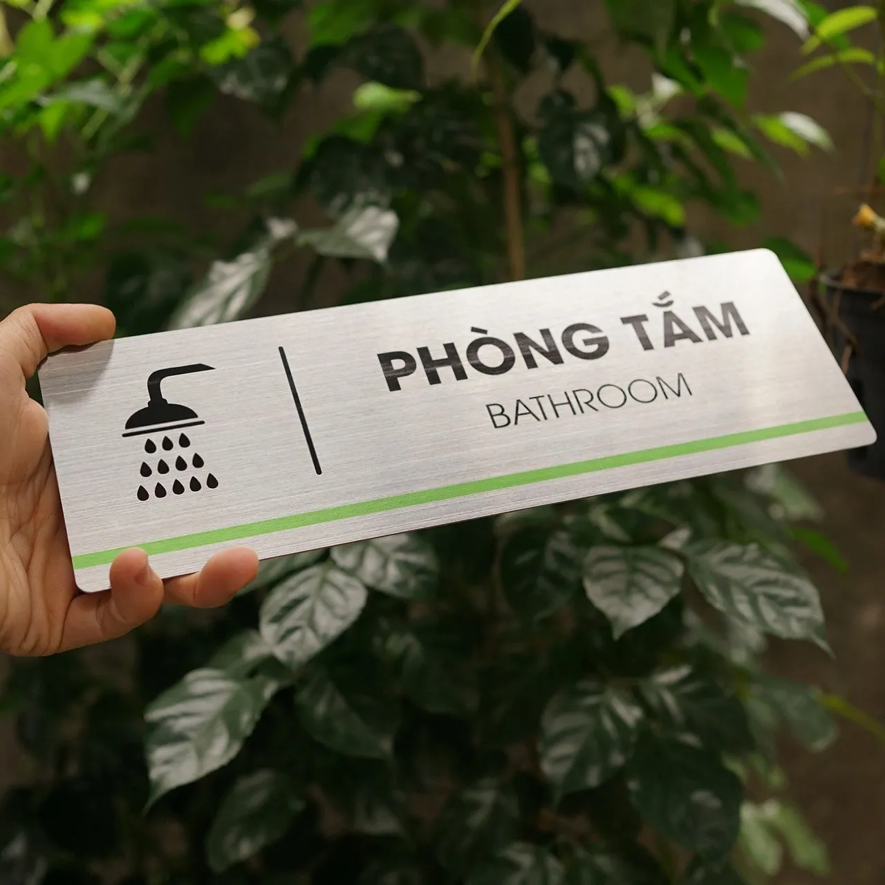 Bảng tên phòng tắm inox 304 cầm tay toàn cảnh – thấy rõ tỷ lệ và bề mặt Bảng tên phòng tắm inox 304 phay xước cầm tay toàn cảnh mặt trước nền cây xanh tối