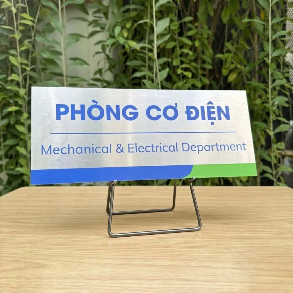 Bảng tên phòng cơ điện inox 304 đặt trên giá đỡ inox, nền cây xanh ngoài trời