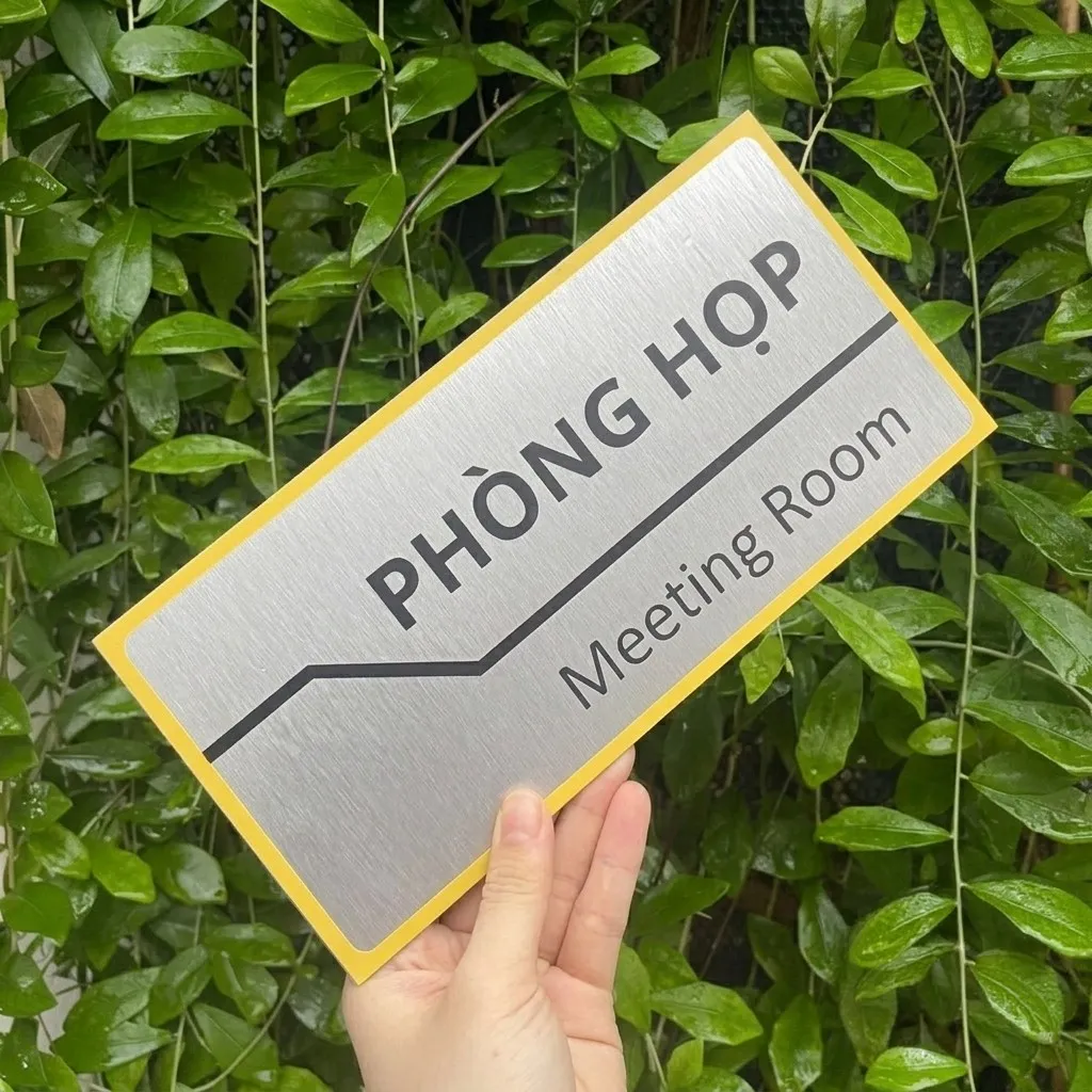 Bảng tên phòng họp viền vàng cầm nghiêng trên nền cây xanh