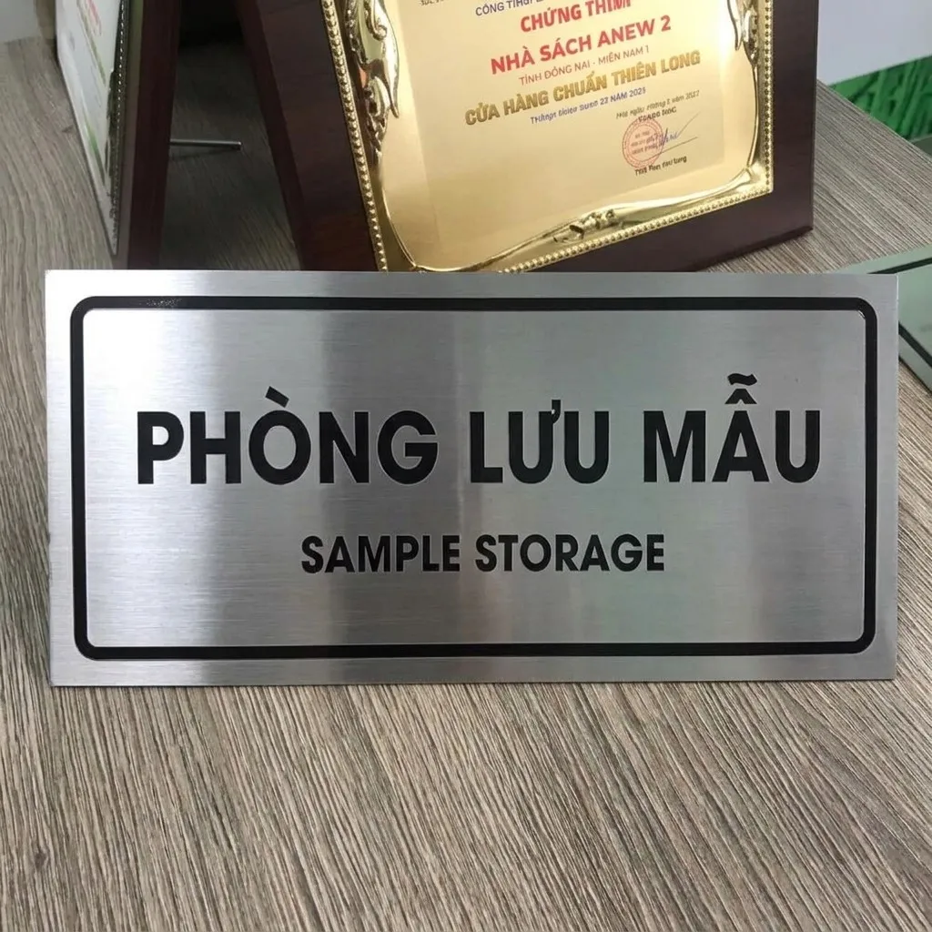 Bảng Tên Phòng Lưu Mẫu Inox – Phối Cảnh Thực Tế Tại Cửa Hàng bảng tên phòng lưu mẫu inox đặt trên bàn cùng bằng khen thực tế tại cửa hàng