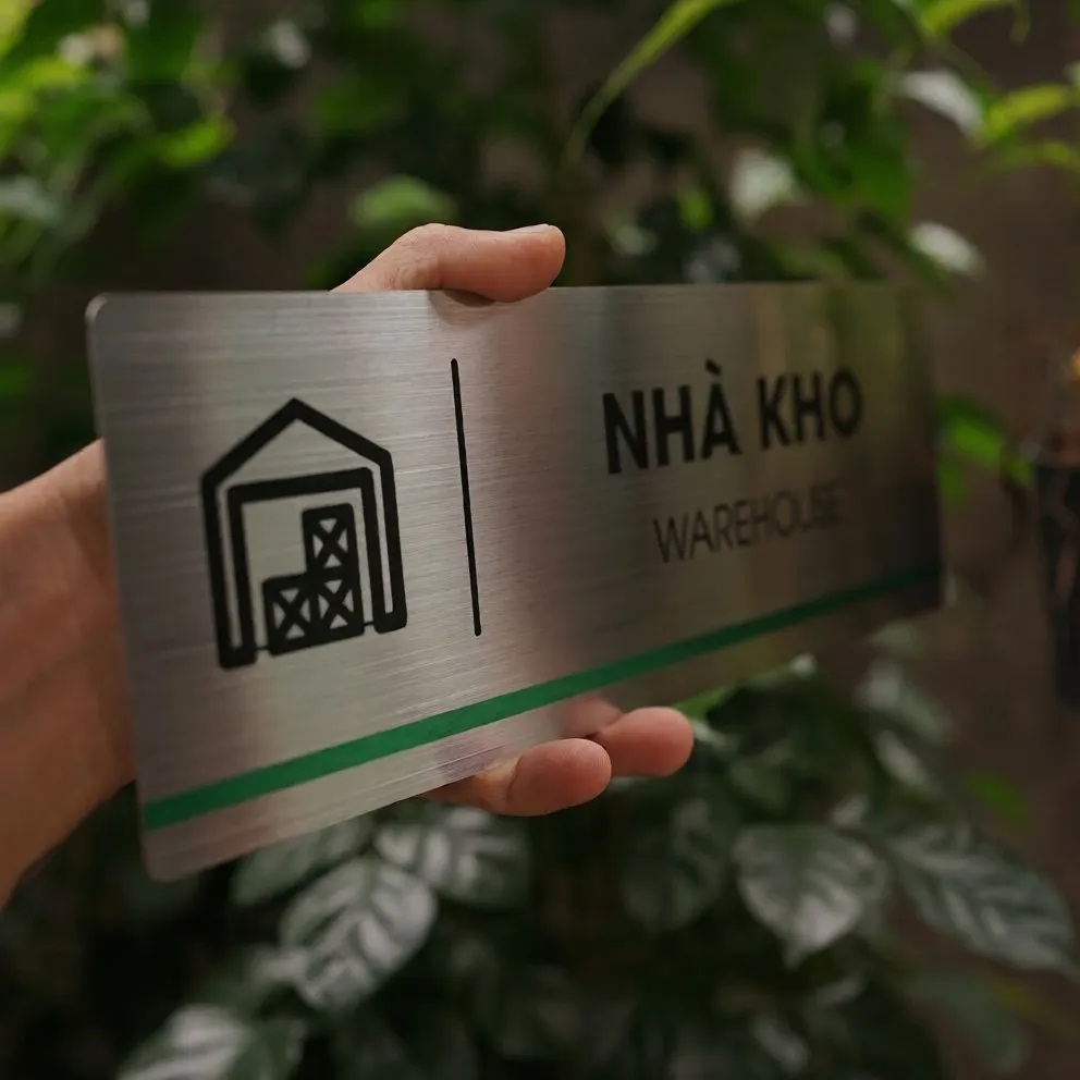 Cận cảnh pictogram nhà kho ăn mòn hóa học sắc nét trên nền inox 304 phay xước bảng hiệu vàng
