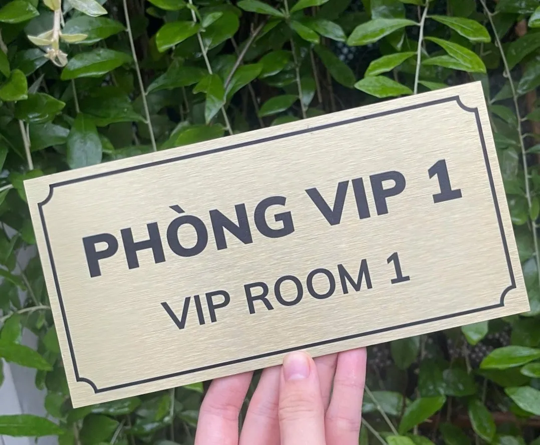 Bảng tên phòng VIP inox vàng xước cầm tay góc nghiêng nền lá xanh