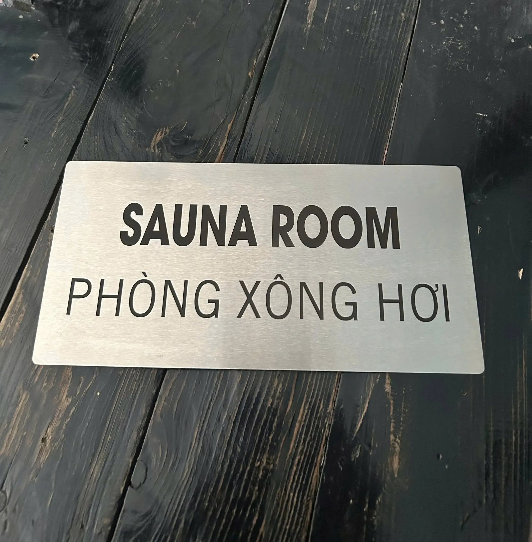 Biển Sauna Room - Phòng Xông Hơi inox bạc xước Biển Sauna Room - Phòng Xông Hơi inox bạc xước song ngữ Anh Việt trên nền gỗ