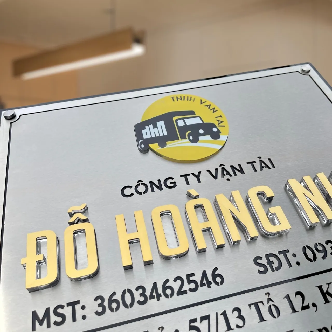 Cận cảnh chữ nổi 3D inox vàng gương dày 15mm và logo công ty vận tải in UV đính nổi trên bảng hiệu inox xước bạc