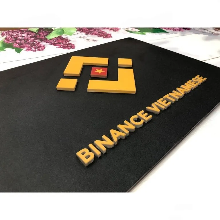 Cận cảnh logo và chữ mica nổi 3D màu vàng trên nền inox đen matte hạt mịn Cận cảnh logo mica hút định hình nổi 3D màu vàng cam và chữ mica nổi 3D trên nền inox sơn tĩnh điện đen matte – bảng hiệu công ty 3D