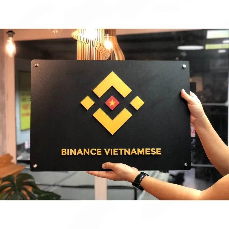 Phối cảnh thực tế bảng hiệu công ty inox đen matte logo mica nổi 3D – Bảng Hiệu Vàng Phối cảnh thực tế bảng hiệu công ty inox đen matte hạt mịn, logo mica nổi 3D vàng cam tương phản mạnh, cầm tay thực tế