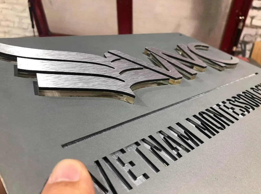Chi tiết logo nổi 3D inox bạc xước trên bảng hiệu công ty xám khói Cận cảnh logo nổi 3D inox bạc xước và viền cạnh sắc nét trên bảng hiệu công ty – Bảng Hiệu Vàng