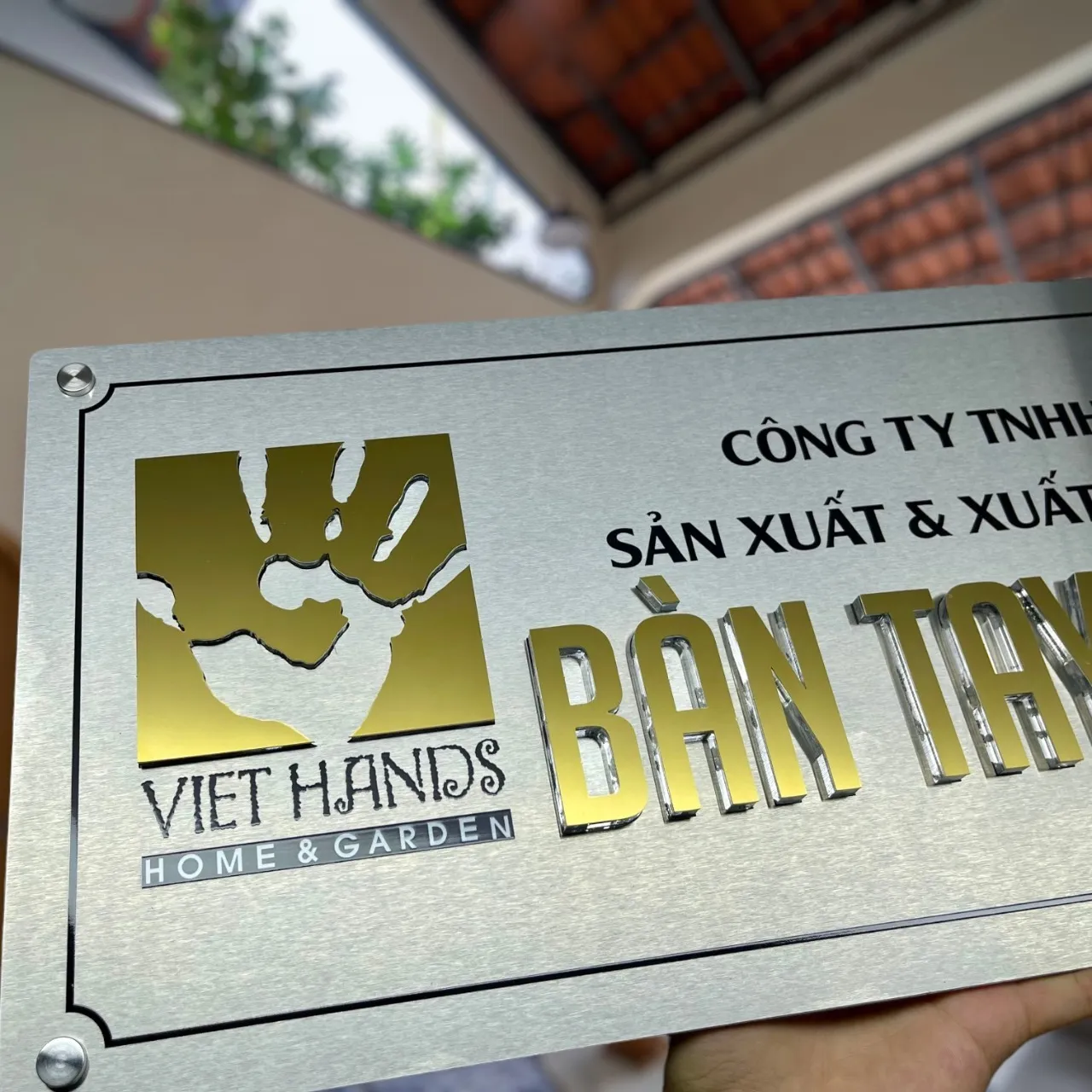 Cận cảnh logo Viet Hands và chữ nổi BÀN TAY inox vàng gương 3D trên nền inox trắng xước