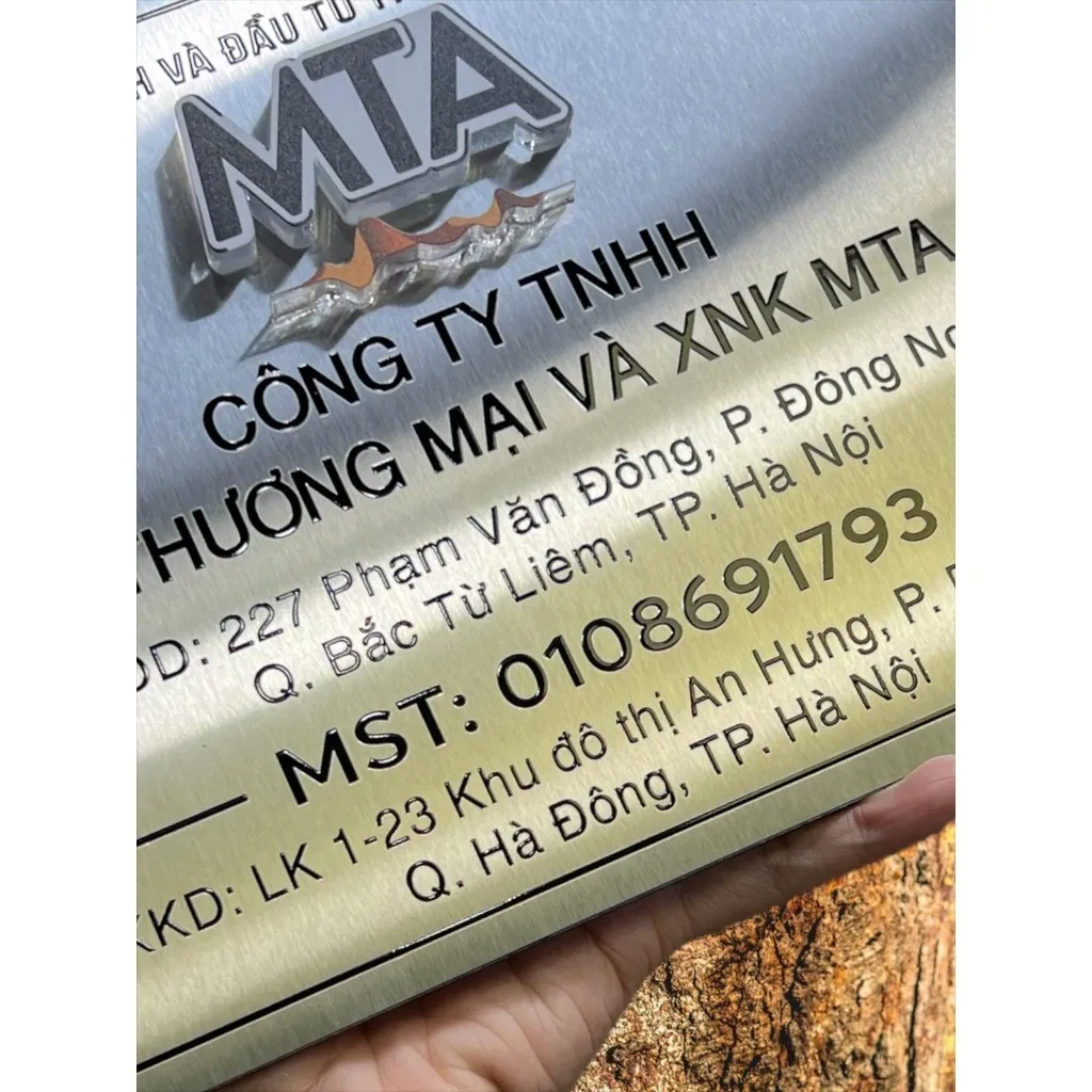 Cận cảnh logo MTA chrome và chữ đen in UV trên nền inox trắng xước – bảng hiệu công ty in UV màu sắc tùy chỉnh