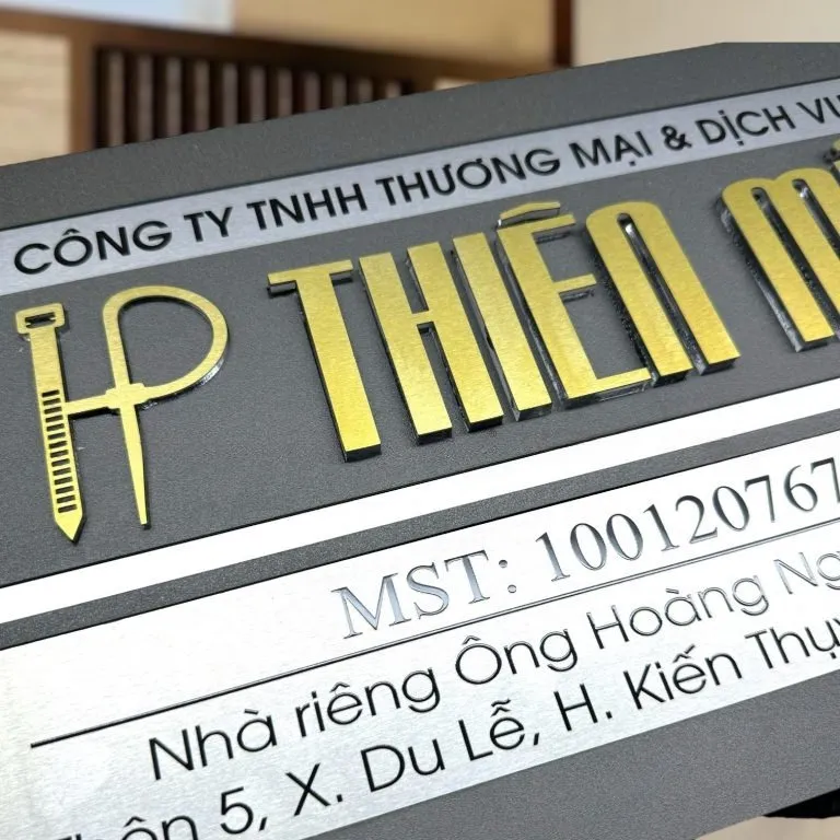 Cận cảnh chữ nổi 3D inox vàng và logo trên bảng hiệu công ty xám khói Cận cảnh chữ nổi 3D inox vàng xước và logo dựng inox trên bảng hiệu công ty xám khói bạc 2 lớp