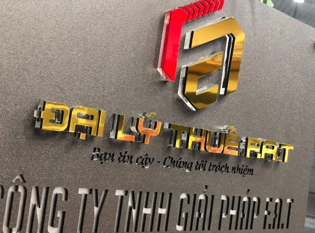 Cận cảnh logo nổi 3D đa màu vàng đỏ bạc trên bảng hiệu công ty inox xám khói Cận cảnh logo 3D inox đa màu vàng gương đỏ bạc gương nổi trên nền inox xám khói sơn tĩnh điện mịn