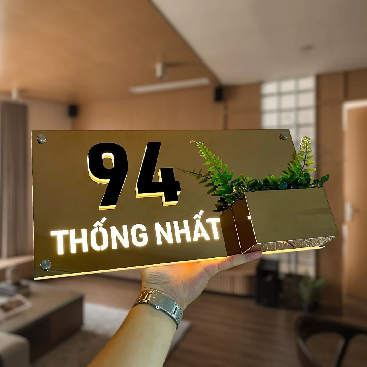 Bảng số nhà inox vàng gương tích hợp chậu cây — mặt trước LED halo bật đầy đủ Bảng số nhà inox vàng gương tích hợp chậu cây xanh mặt trước LED halo vàng ấm bật sáng đầy đủ