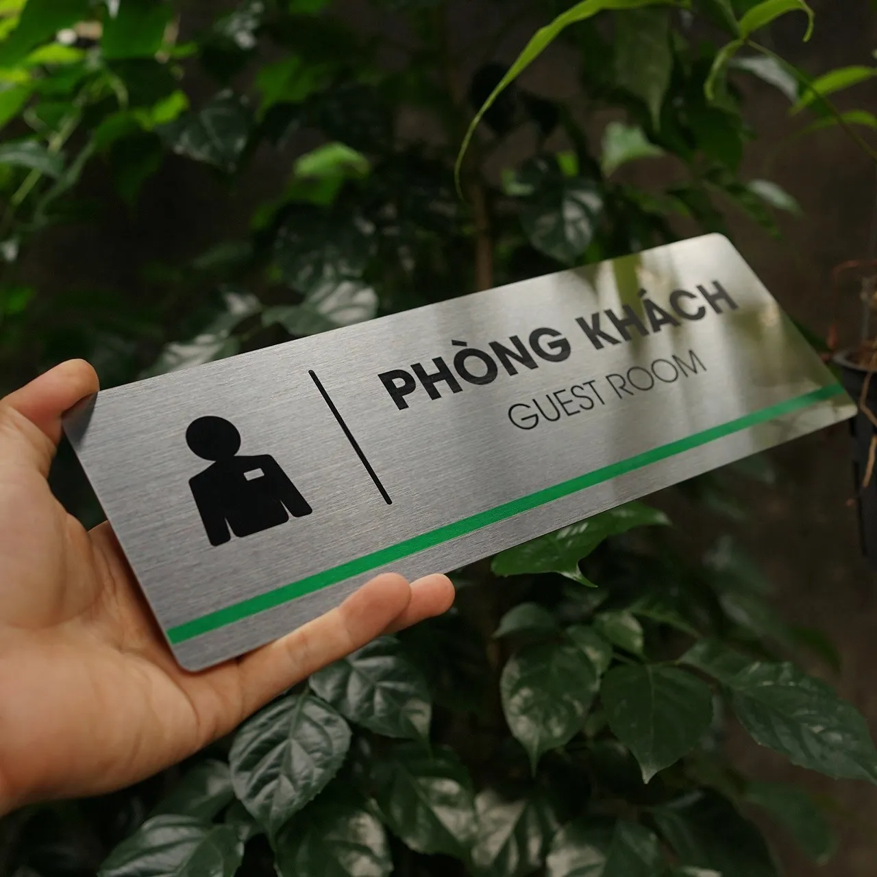 Bảng tên phòng khách inox 304 phay xước cầm tay góc nghiêng trái ánh kim bề mặt nền lá tối