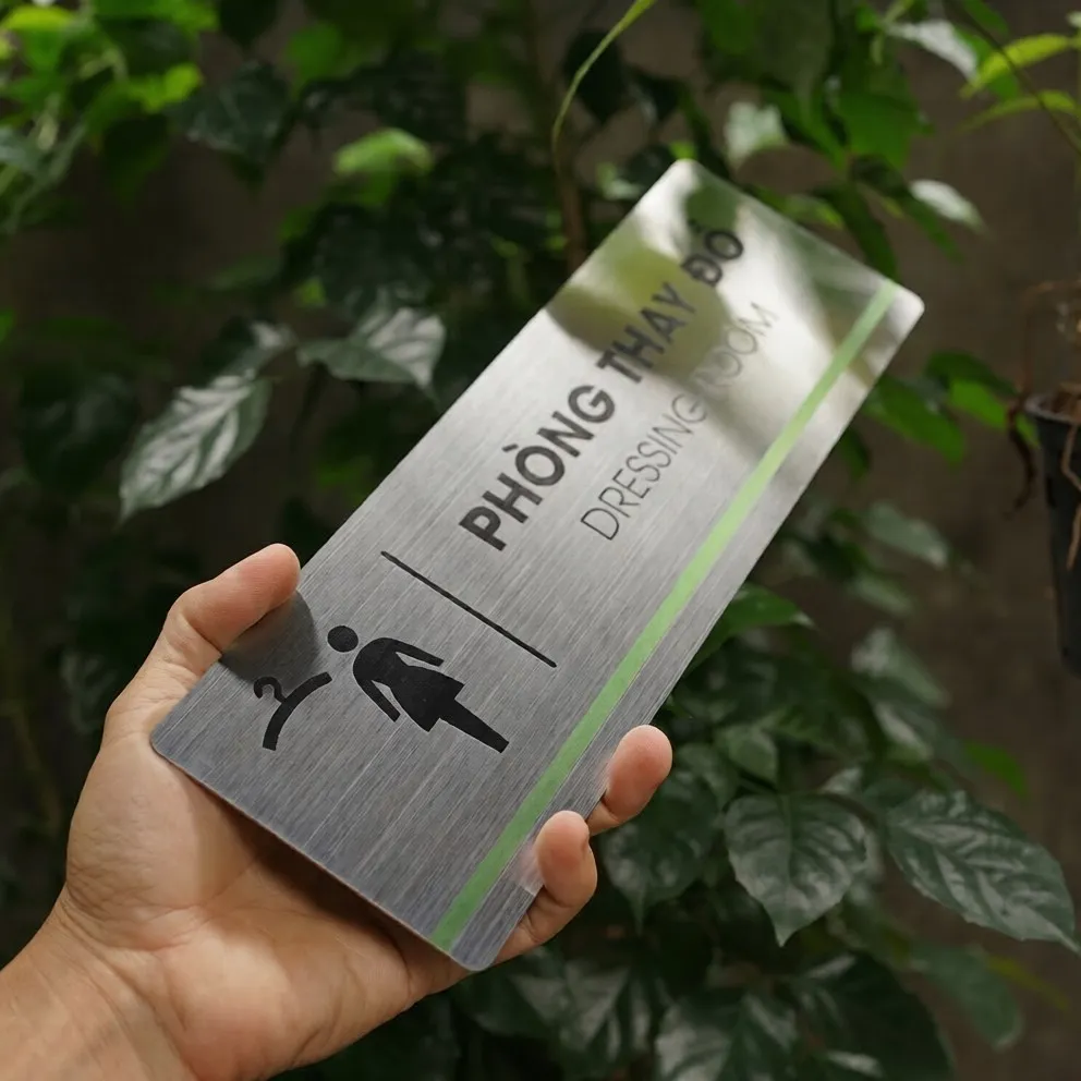 Cận cảnh pictogram phòng thay đồ móc áo và nhân vật nữ ăn mòn hóa học sắc nét trên inox 304 phay xước góc nghiêng