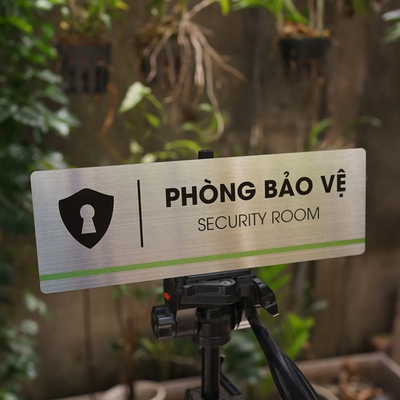 Phối cảnh bảng tên phòng bảo vệ inox 304 ngoài trời – Bảng Hiệu Vàng Bảng tên phòng bảo vệ inox 304 brushed đặt ngoài trời trên giá tripod, ánh sáng ban ngày