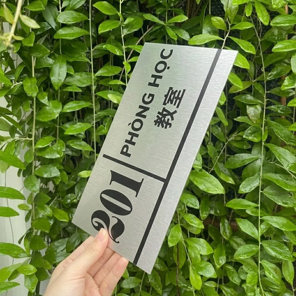 Bảng tên phòng học song ngữ cầm tay theo chiều dọc trên nền cây xanh