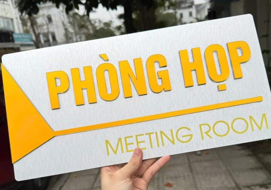 Cận cảnh chữ mica nổi và tam giác định hướng trên bảng phòng họp Cận cảnh chữ mica nổi in UV vàng cam và khối tam giác mũi tên trên bảng phòng họp inox