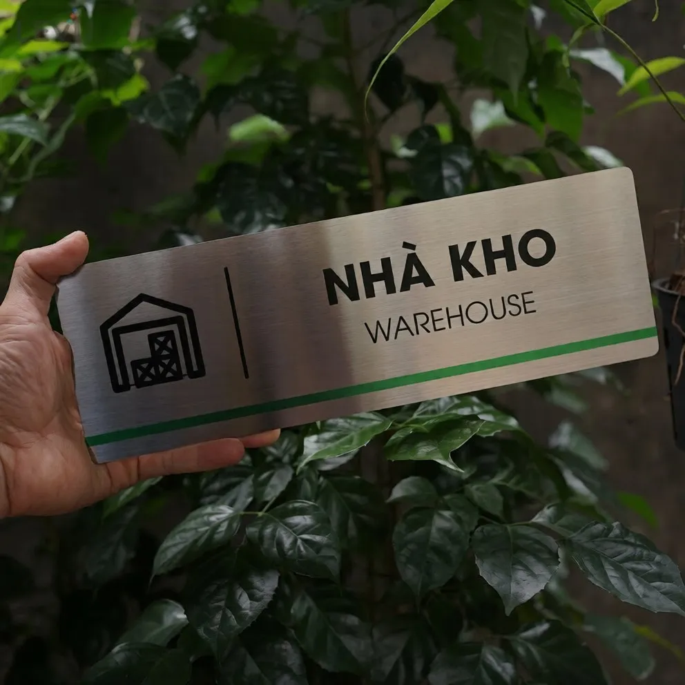 Cầm tay bảng tên nhà kho inox 304 phay xước mặt trước thấy rõ chữ ăn mòn hóa học và pictogram kho