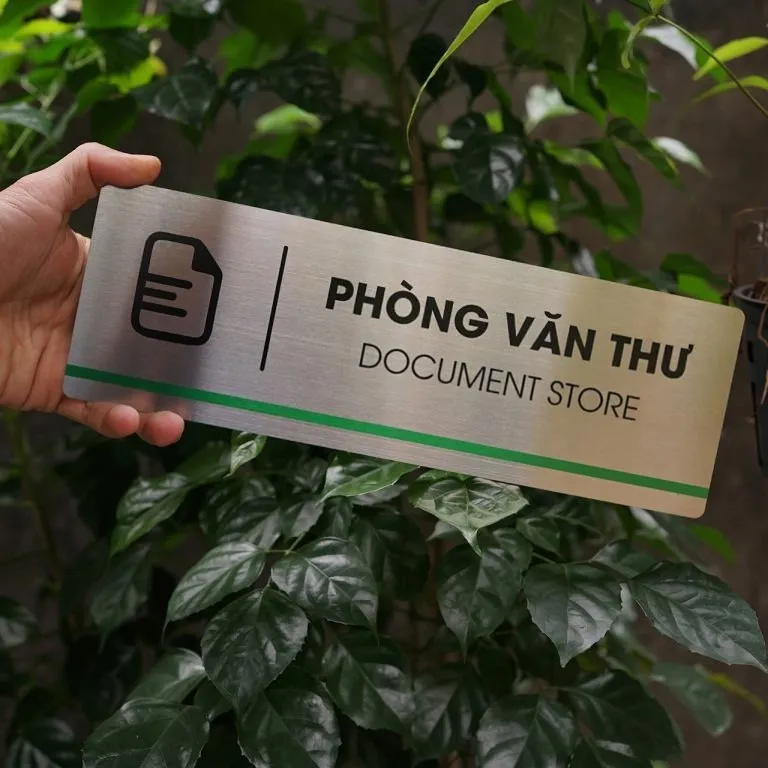 Bảng tên phòng văn thư inox 304 phay xước cầm tay mặt trước nền cây xanh đậm