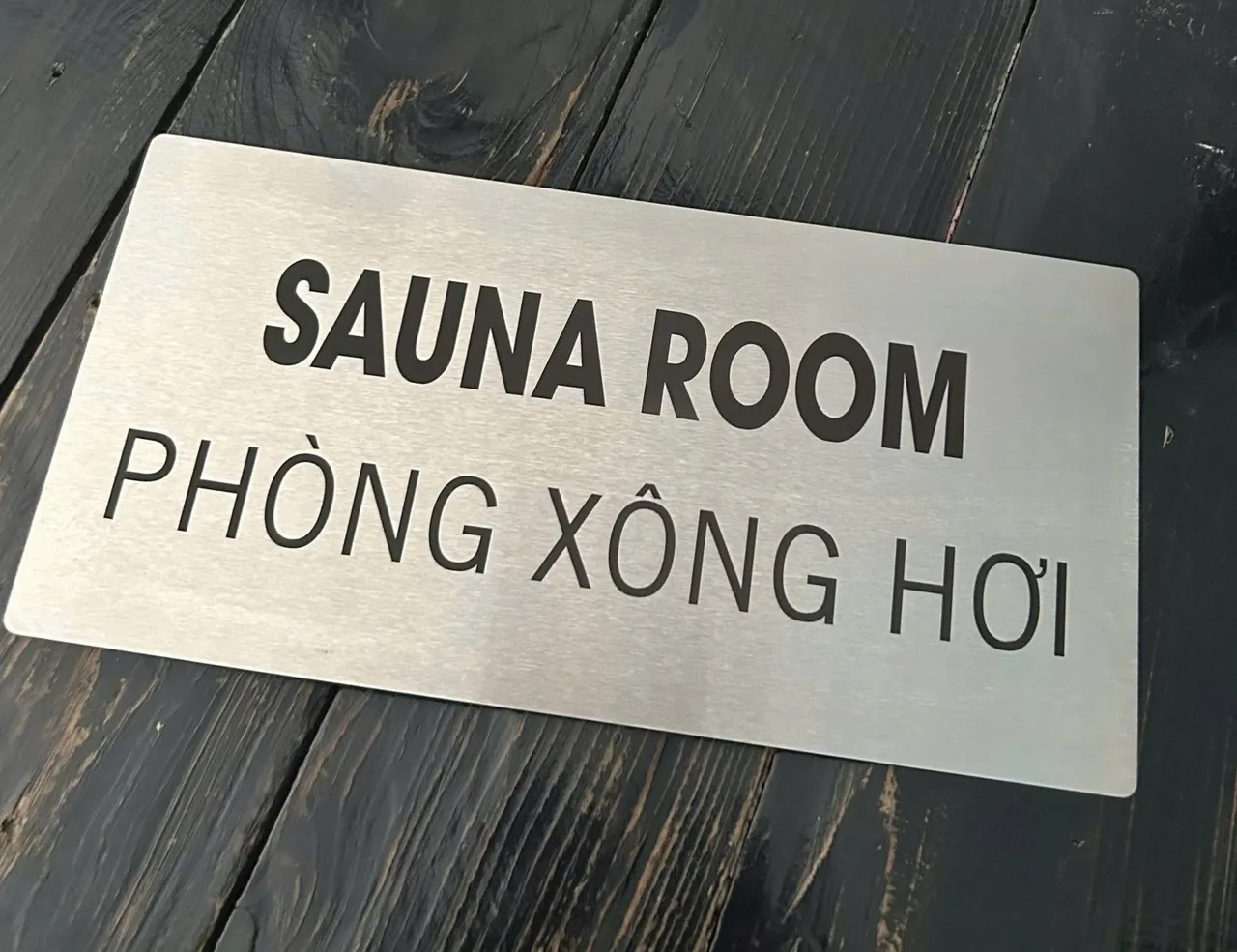 Cận cảnh biển Sauna Room inox bạc xước Cận cảnh biển Sauna Room - Phòng Xông Hơi inox bạc xước hairline trên nền gỗ
